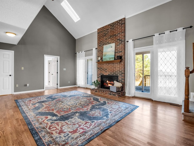 living room with wood finished floors, baseboards, high vaulted ceiling, a skylight, and a brick fireplace