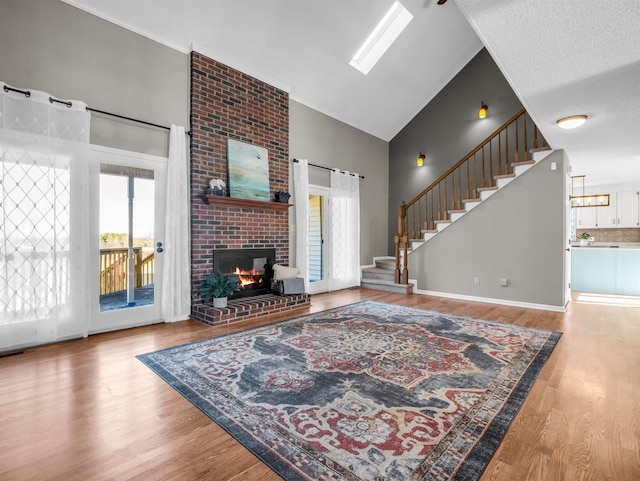 living area with stairway, a brick fireplace, high vaulted ceiling, and wood finished floors