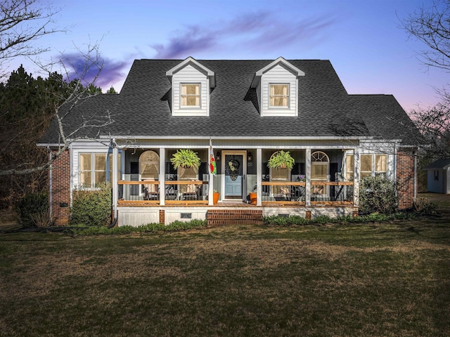 cape cod home featuring a lawn, a porch, brick siding, and a shingled roof