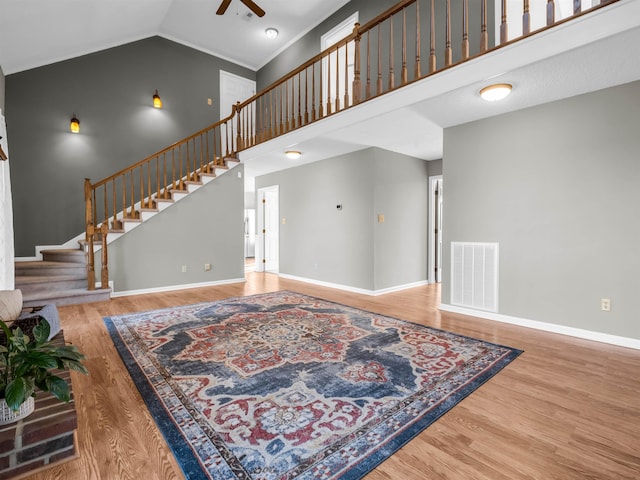 living area featuring visible vents, high vaulted ceiling, wood finished floors, baseboards, and stairs