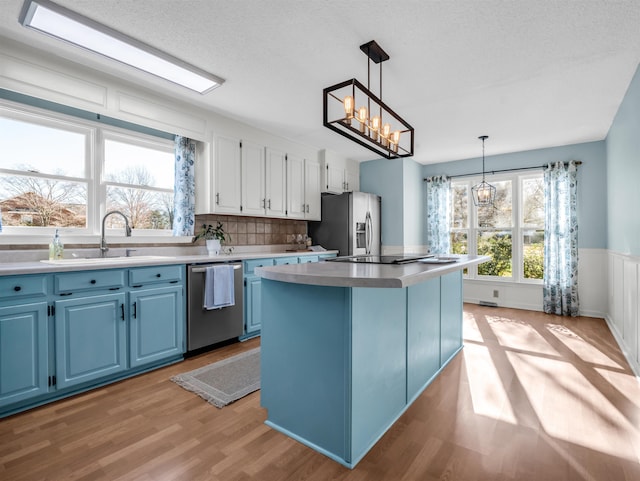 kitchen featuring a kitchen island, a notable chandelier, stainless steel appliances, blue cabinets, and a sink