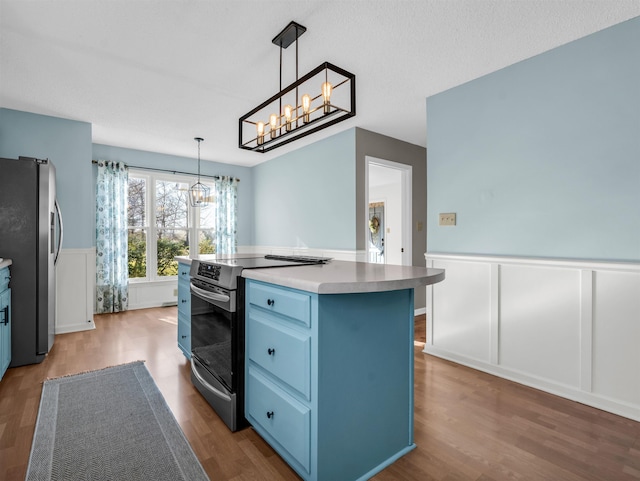 kitchen with blue cabinetry, a wainscoted wall, wood finished floors, a decorative wall, and stainless steel appliances