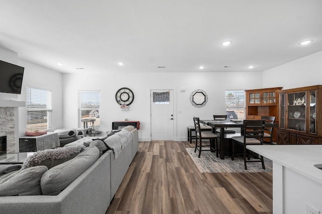 living room with a stone fireplace, dark wood-type flooring, recessed lighting, and baseboards