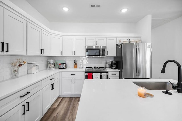 kitchen featuring wood finished floors, visible vents, a sink, stainless steel appliances, and backsplash