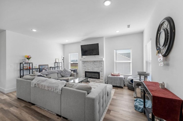 living room with a stone fireplace, recessed lighting, and wood finished floors