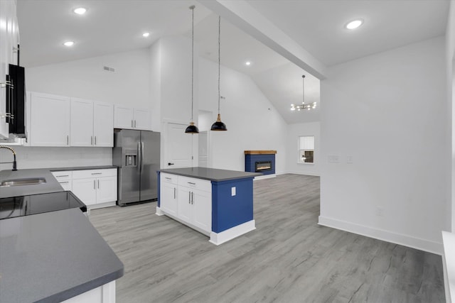 kitchen with dark countertops, stainless steel fridge with ice dispenser, a warm lit fireplace, light wood-style floors, and a sink