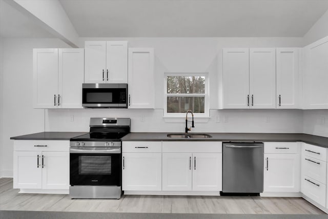 kitchen with a sink, stainless steel appliances, dark countertops, and white cabinetry