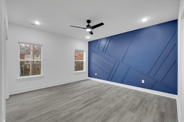 spare room with baseboards, wood finished floors, a ceiling fan, and a decorative wall