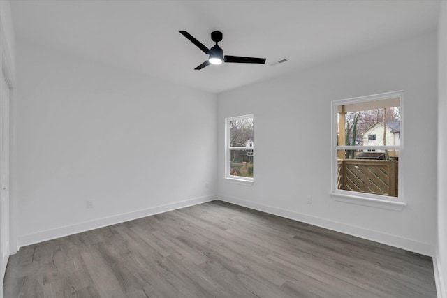 empty room with ceiling fan, visible vents, baseboards, and wood finished floors