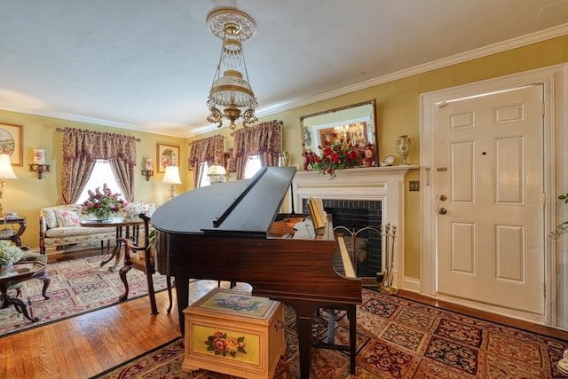 living area with a notable chandelier, a brick fireplace, wood finished floors, and crown molding