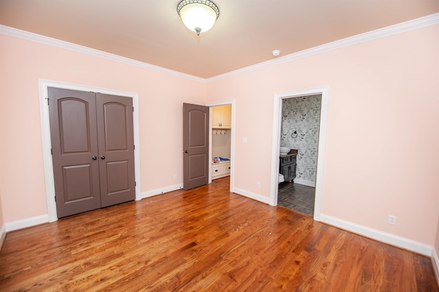 unfurnished bedroom featuring baseboards, ornamental molding, wood finished floors, a closet, and ensuite bath