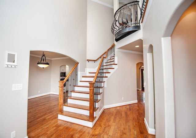 stairway featuring wood finished floors, arched walkways, a towering ceiling, and baseboards