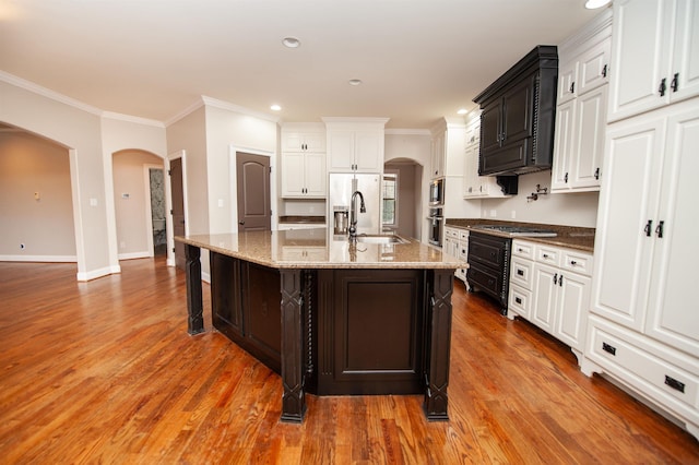 kitchen featuring a sink, arched walkways, crown molding, and light wood finished floors