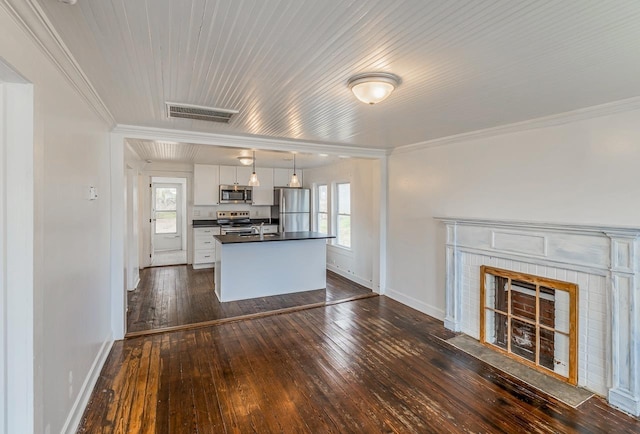 kitchen with dark wood-style flooring, stainless steel appliances, white cabinets, a tiled fireplace, and dark countertops