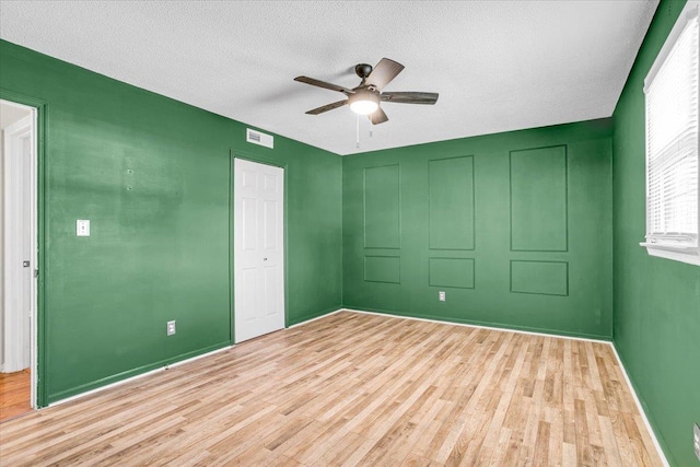 unfurnished room featuring a ceiling fan, baseboards, visible vents, light wood finished floors, and a textured ceiling