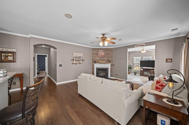 living area with ornamental molding, a glass covered fireplace, dark wood finished floors, arched walkways, and baseboards