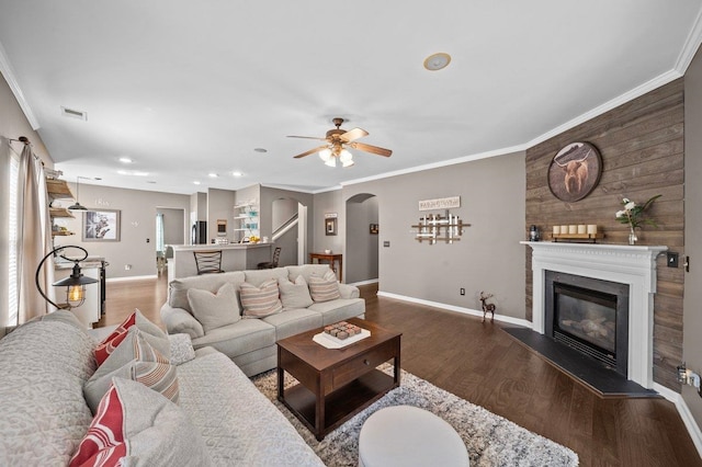 living area with a glass covered fireplace, crown molding, wood finished floors, and arched walkways