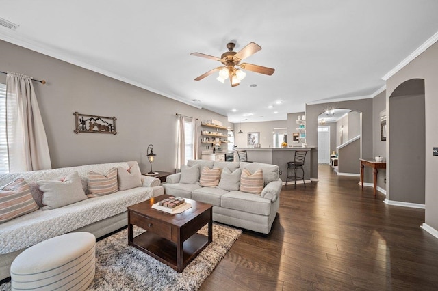 living area featuring dark wood-style floors, baseboards, arched walkways, ornamental molding, and ceiling fan