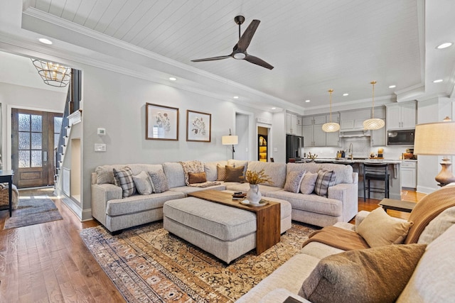 living room featuring recessed lighting, light wood-type flooring, a tray ceiling, and ornamental molding