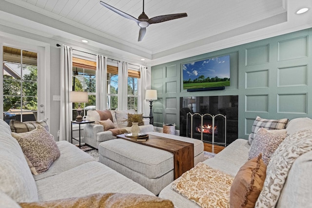 living room featuring ornamental molding, a warm lit fireplace, wood finished floors, a decorative wall, and wood ceiling