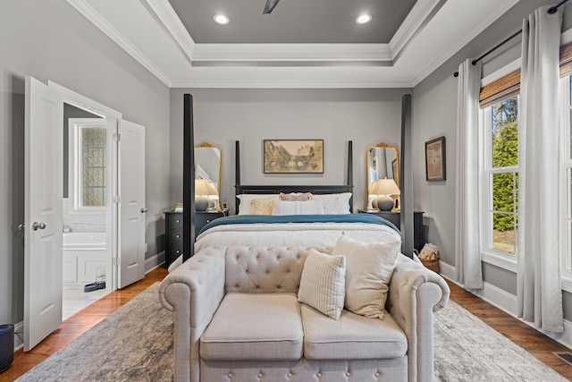 bedroom with a tray ceiling, wood finished floors, ensuite bathroom, and crown molding