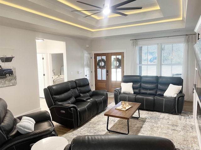 living area featuring wood finished floors, a tray ceiling, ceiling fan, french doors, and crown molding