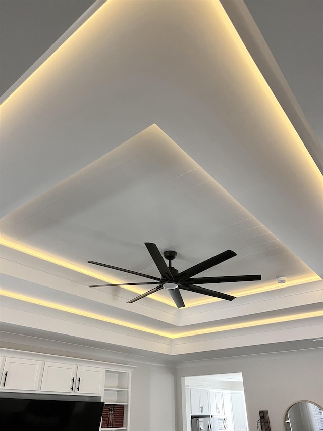 interior details with a ceiling fan and a tray ceiling