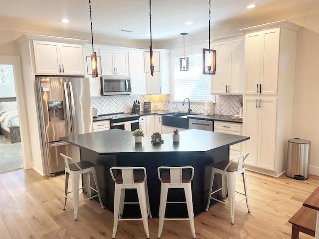 kitchen featuring light wood-type flooring, a sink, dark countertops, stainless steel appliances, and a breakfast bar area