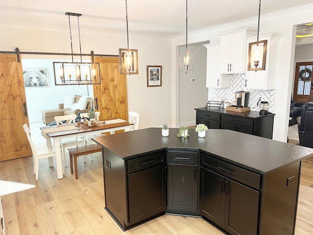 kitchen with light wood-type flooring, ornamental molding, dark countertops, backsplash, and a barn door