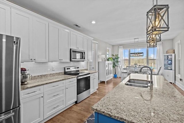 kitchen with decorative backsplash, appliances with stainless steel finishes, wood finished floors, white cabinets, and a sink