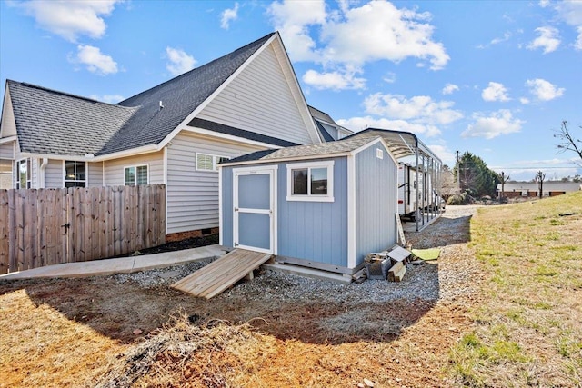 back of house with a shingled roof, a storage shed, an outdoor structure, and fence