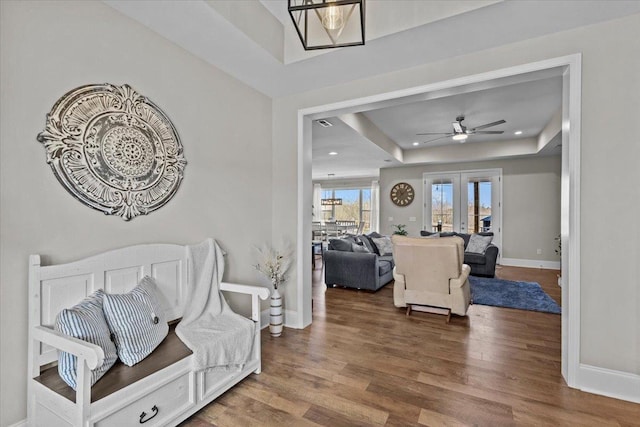 living area with a raised ceiling, wood finished floors, baseboards, and french doors