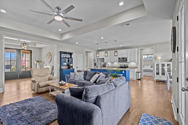 living room featuring a ceiling fan, visible vents, a tray ceiling, recessed lighting, and light wood-type flooring