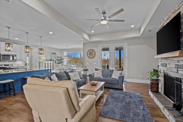 living area featuring a tray ceiling, baseboards, a stone fireplace, and dark wood finished floors