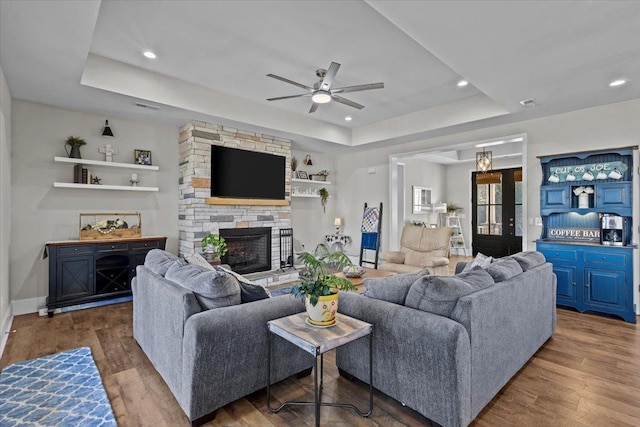 living room with a tray ceiling, baseboards, a stone fireplace, and wood finished floors