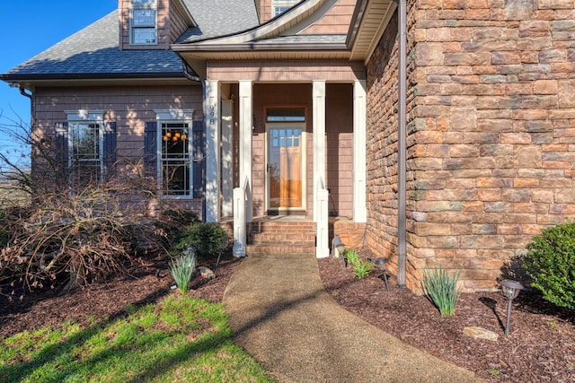 view of exterior entry with stone siding and a shingled roof