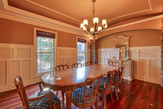 dining space with dark wood finished floors, ornamental molding, a raised ceiling, a decorative wall, and a notable chandelier