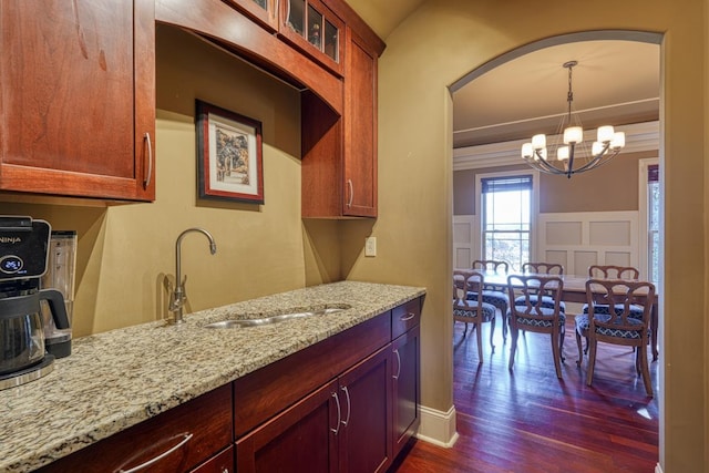 kitchen featuring glass insert cabinets, light stone countertops, dark wood-style floors, a decorative wall, and a sink