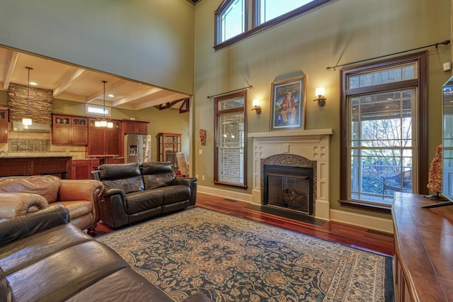 living room featuring beamed ceiling, a fireplace with flush hearth, visible vents, wood finished floors, and baseboards