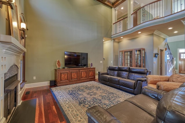 living area featuring baseboards, a fireplace, dark wood-style flooring, a towering ceiling, and crown molding