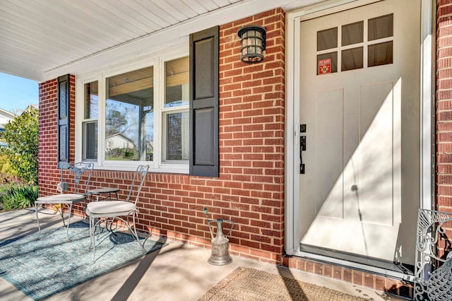 view of exterior entry with brick siding and covered porch