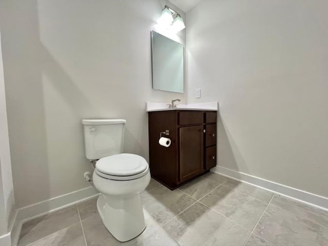 half bath featuring baseboards, toilet, vanity, and tile patterned flooring