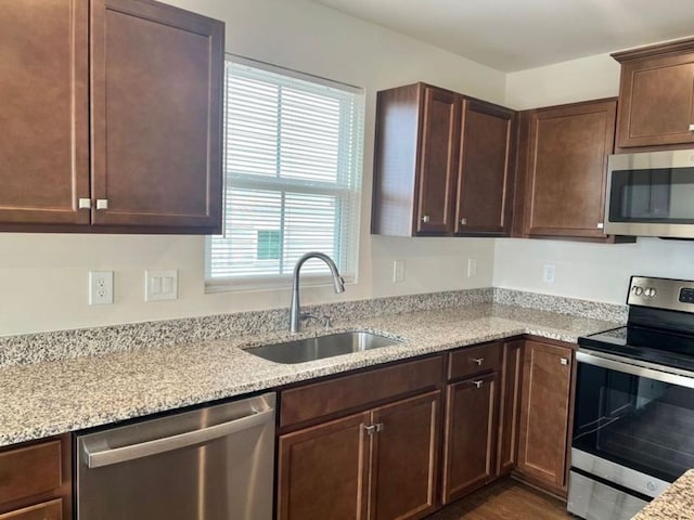 kitchen featuring dark brown cabinetry, appliances with stainless steel finishes, light stone countertops, and a sink