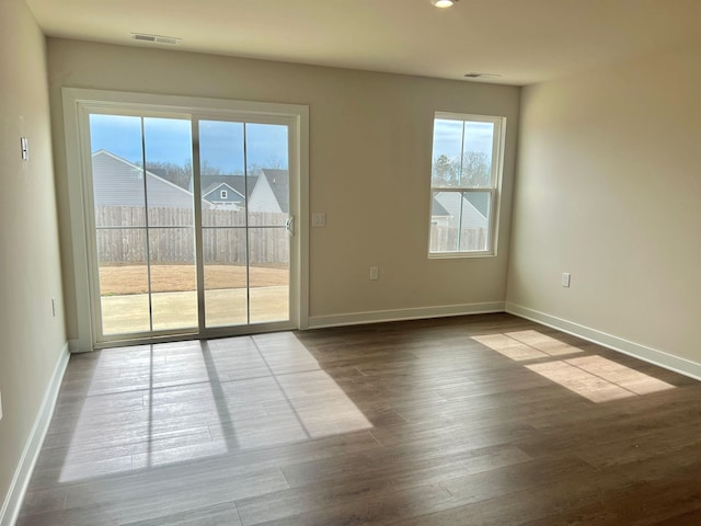 unfurnished room with dark wood-style floors, visible vents, and baseboards