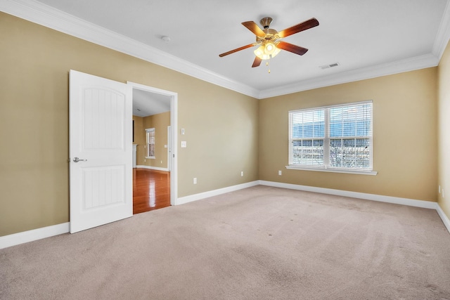 carpeted empty room featuring a ceiling fan, crown molding, baseboards, and visible vents