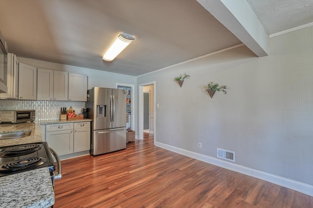 kitchen with tasteful backsplash, visible vents, baseboards, wood finished floors, and stainless steel fridge