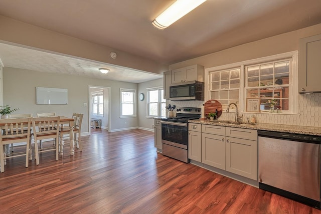 kitchen featuring a sink, backsplash, dark wood-style floors, appliances with stainless steel finishes, and light stone countertops