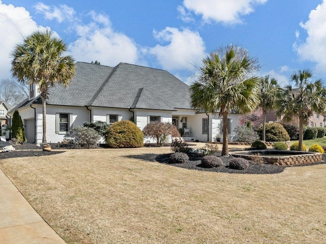 view of front of house featuring a front yard, an attached garage, and a shingled roof