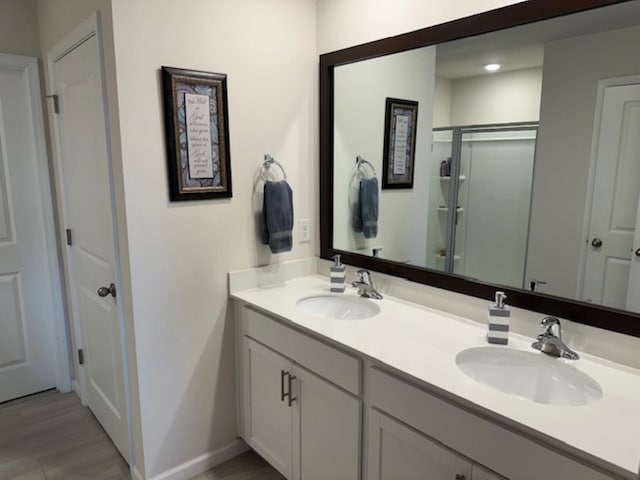 bathroom with double vanity, a stall shower, baseboards, and a sink