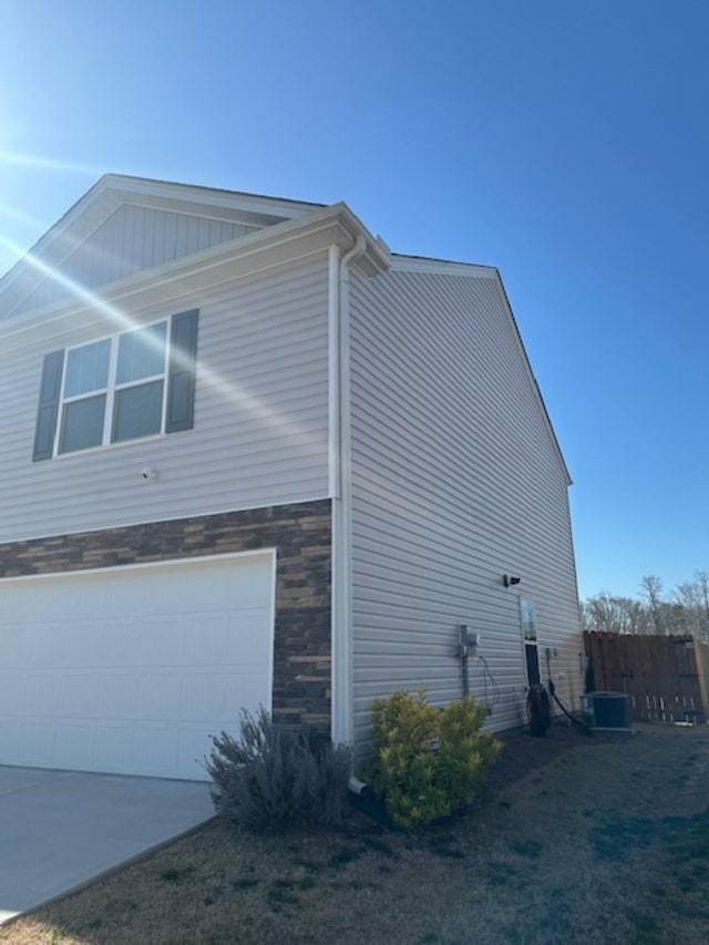 view of home's exterior with an attached garage, fence, stone siding, and central AC